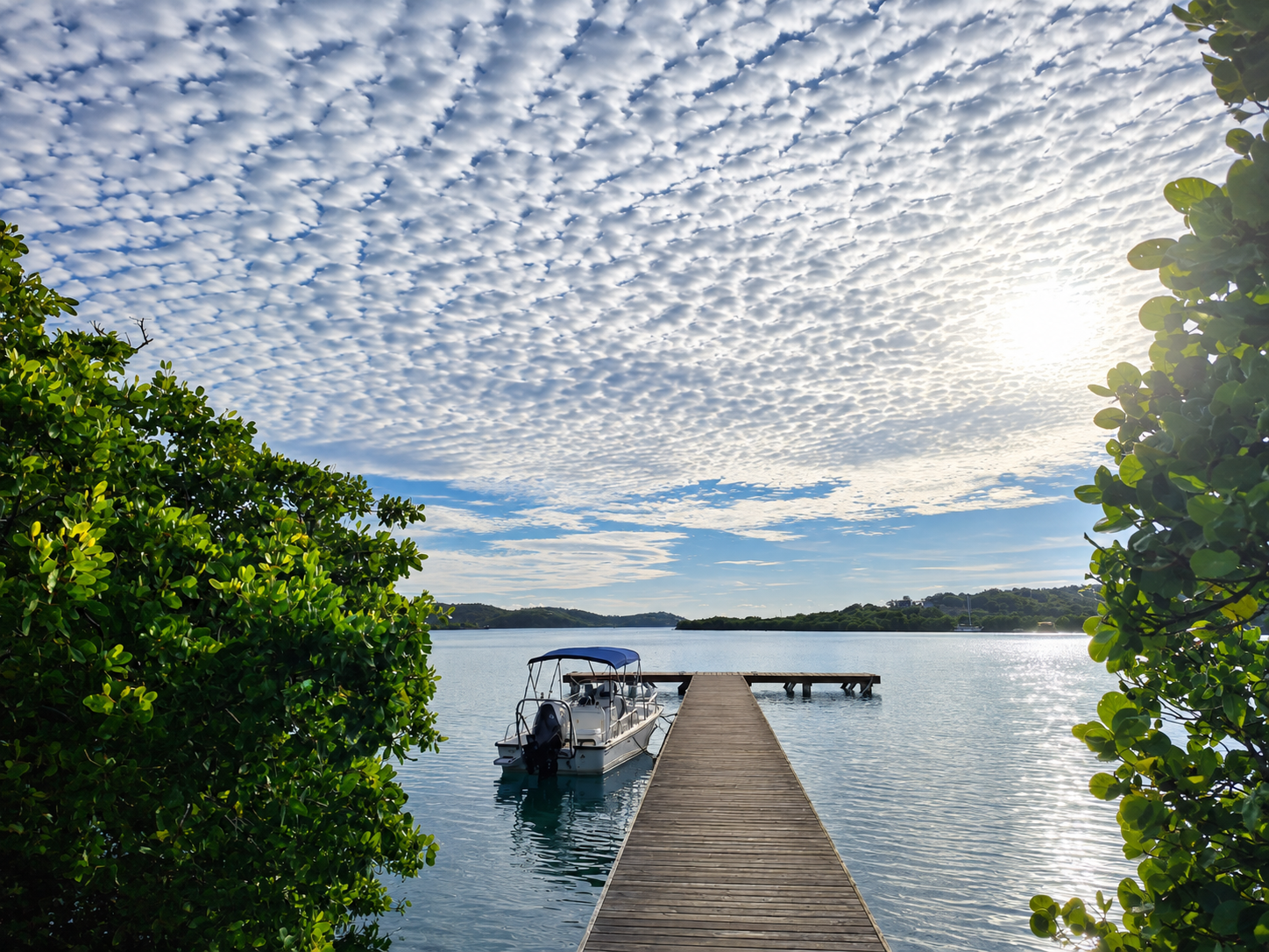 Wooden dock leading into calm Culebra bay waters with a boat under a sky of small white clouds